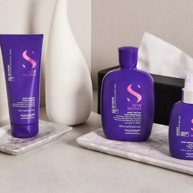 Three purple hair care products on a white surface with a neutral background