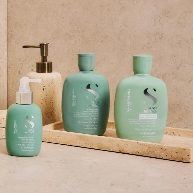 Set of green haircare products on a beige surface with a plant and mirror.