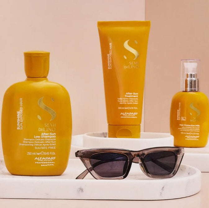 Set of haircare products including bottles and a tube on a white tray with sunglasses, against a beige background.